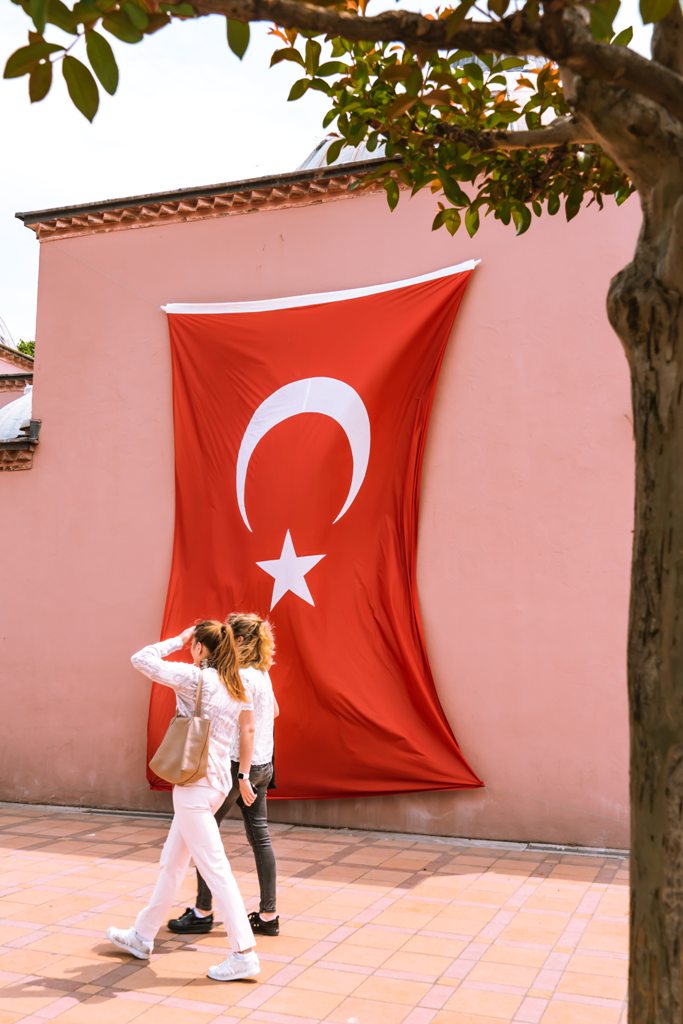 Young woman walking past a Turkish flag. (Photo: Jean Carlo Emer / Unsplash)