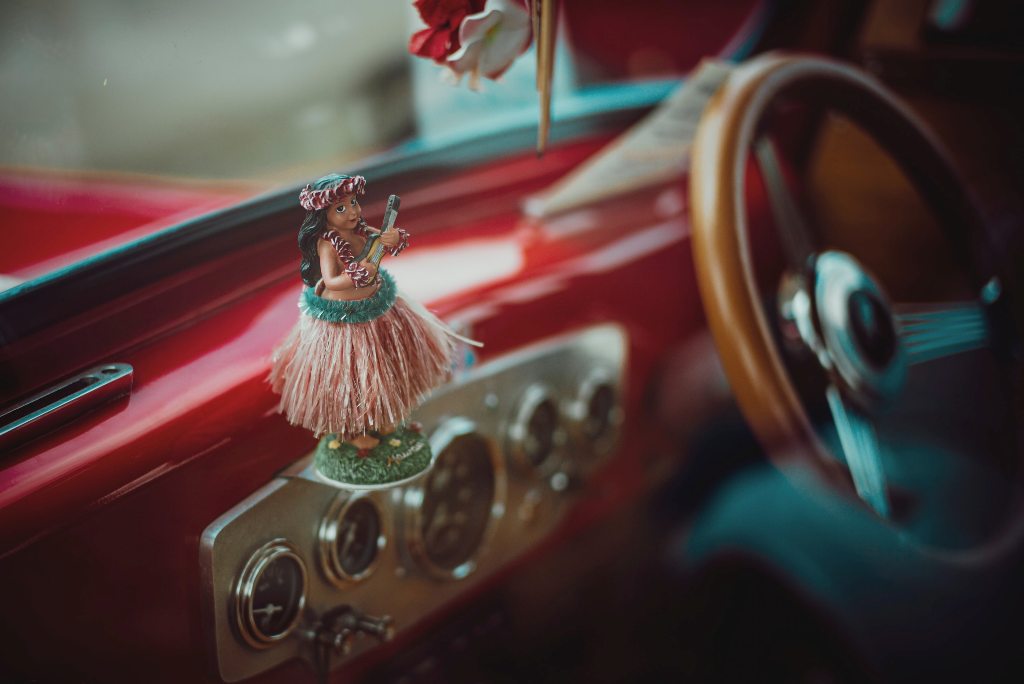 A Hawaiian hula dancer as a doll in a car. (Photo: Aleks Marinkovic / Unsplash)